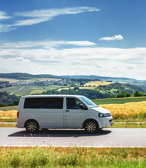 En silvergrå minivan parkerad vid sidan av en landsväg med ett gyllene fält och kullar i bakgrunden