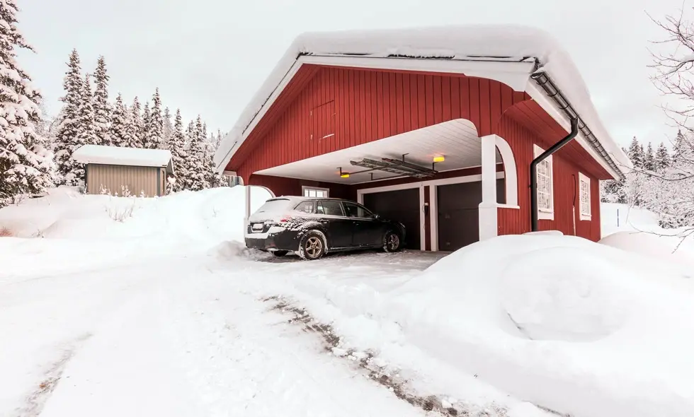 En bil parkerad under ett carport med snötäckt tak och omgivning
