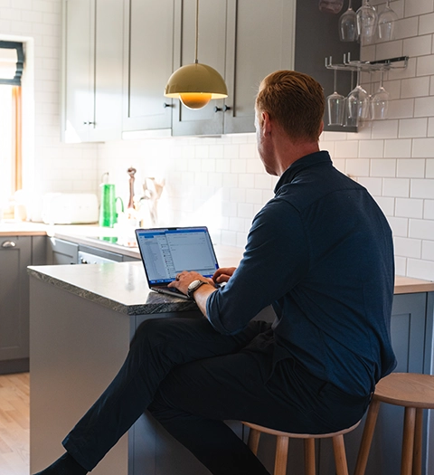 Man sitter vid en köksö och arbetar på en laptop i ett modernt kök.