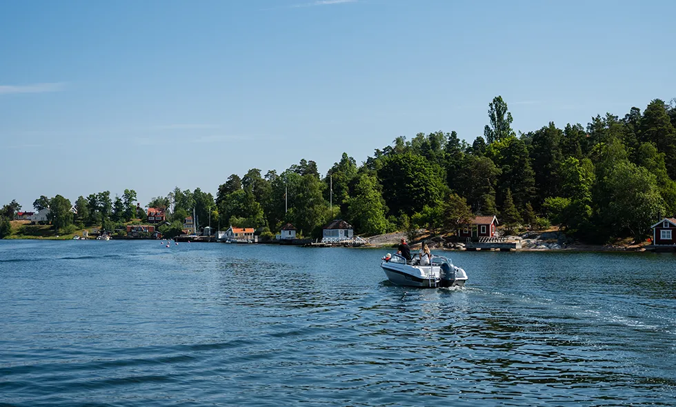 Strandlinje med hus, träd och en båt på sjön.