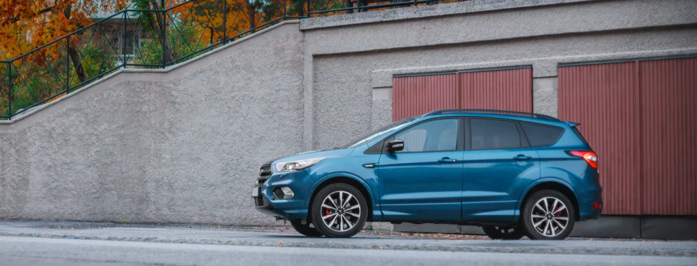 En blå SUV parkerad vid sidan av en gata med röd garagedörr och grå väggar i bakgrunden, tydliga röda och vita reflexer på hju
