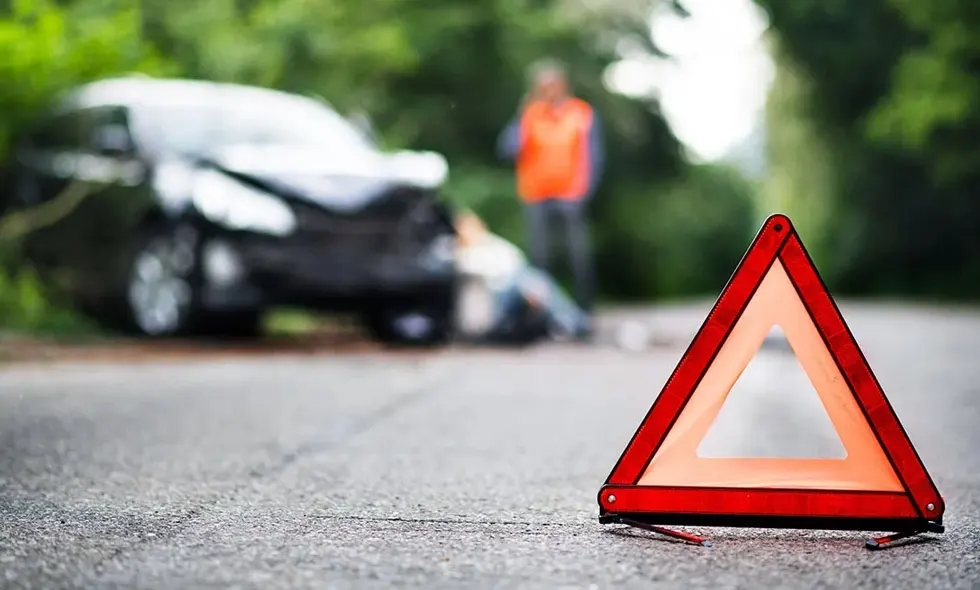 En varningstriangel på vägen framför en bilolycka med en person i bakgrunden