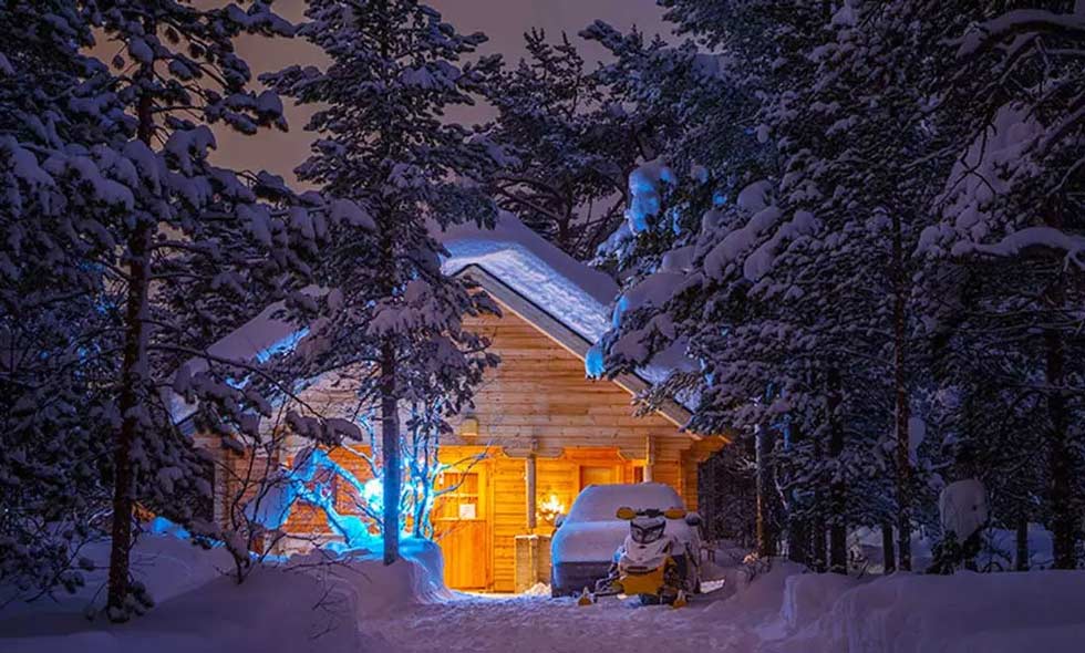 En snöskoter och en bil står framför en stuga i snöklätt landskap.