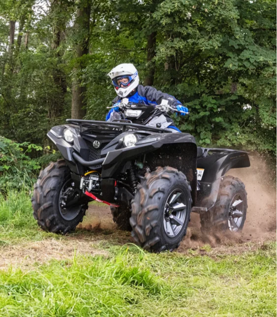 Förare i blå jacka kör svart ATV från Yamaha på skogsstig.