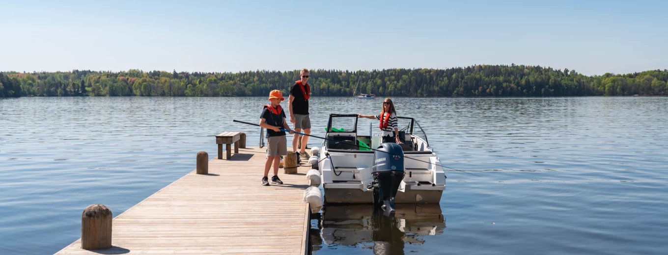 Två personer åker i en motorbåt på ett blått vatten med skärgårdslandskap i bakgrunden