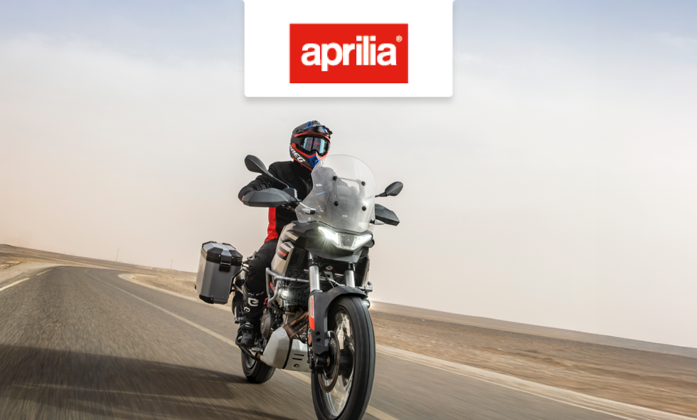 En person som kör en mc av märket Aprilia på en öde landsväg genom ökenlikt landskap.