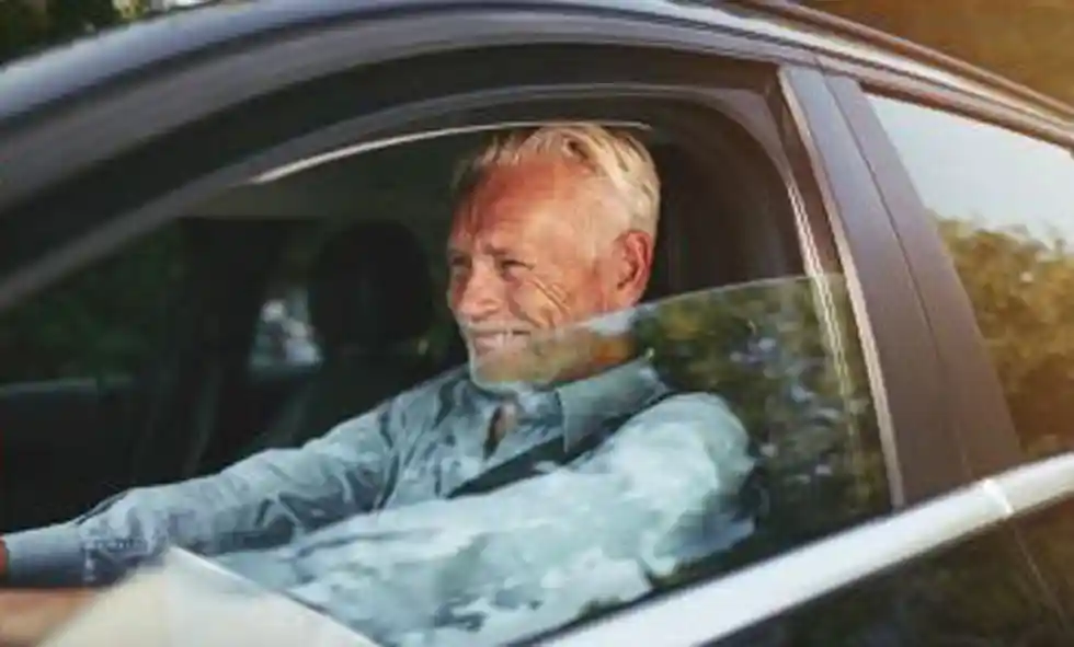 Man sitter framför ratten i en bil och ler.