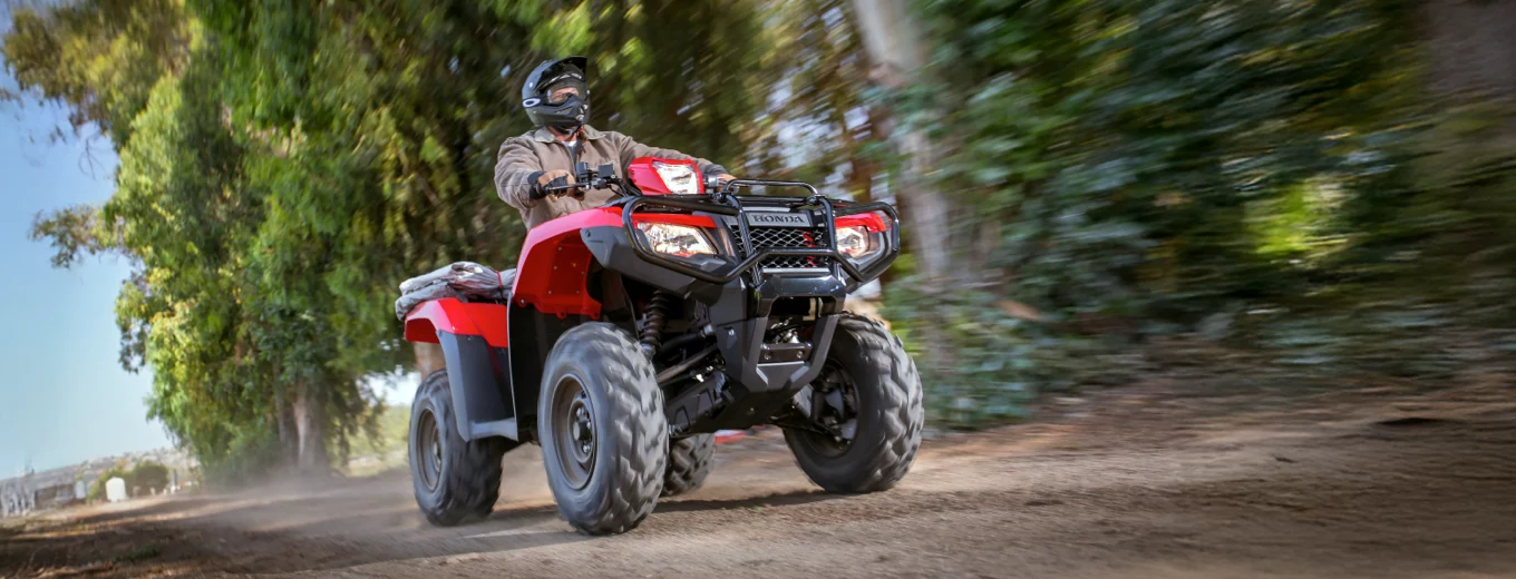 Person kör röd ATV från Honda på grusväg med träd i bakgrunden.