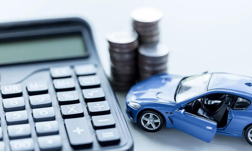 En närbild av en blå miniatyrbil, miniräknare och staplar av mynt som symboliserar bilfinansiering