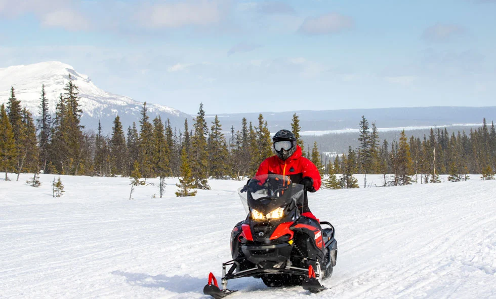 Person i röd jacka kör på snötäckt landskap med fjäll i bakgrunden