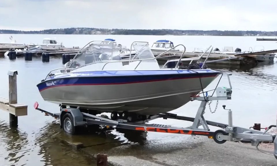 En båt som står på en trailer i ramp ned i vatten.