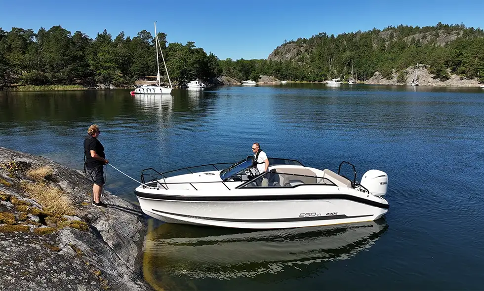 Person som står på klippa med båten framför sig i sjön.