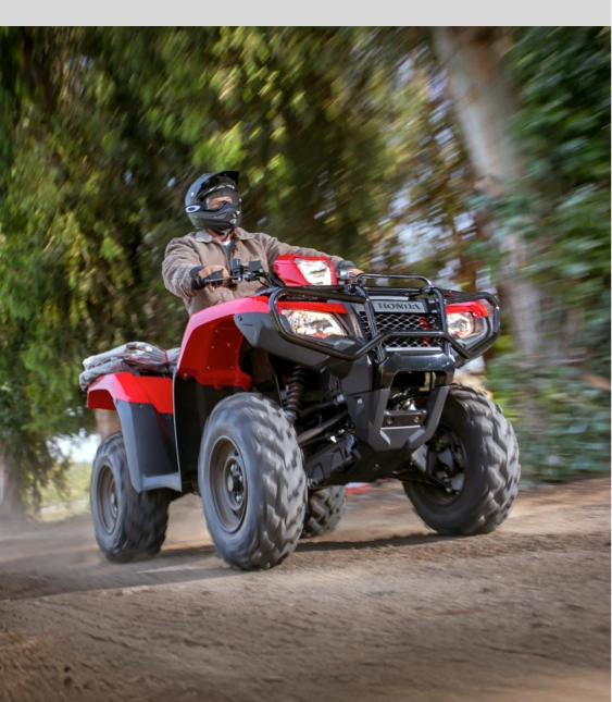 Person kör röd ATV från Honda på grusväg med träd i bakgrunden.