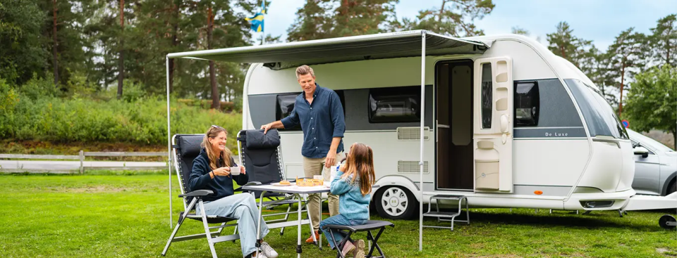 Familj fikar utomhus vid husvagn.