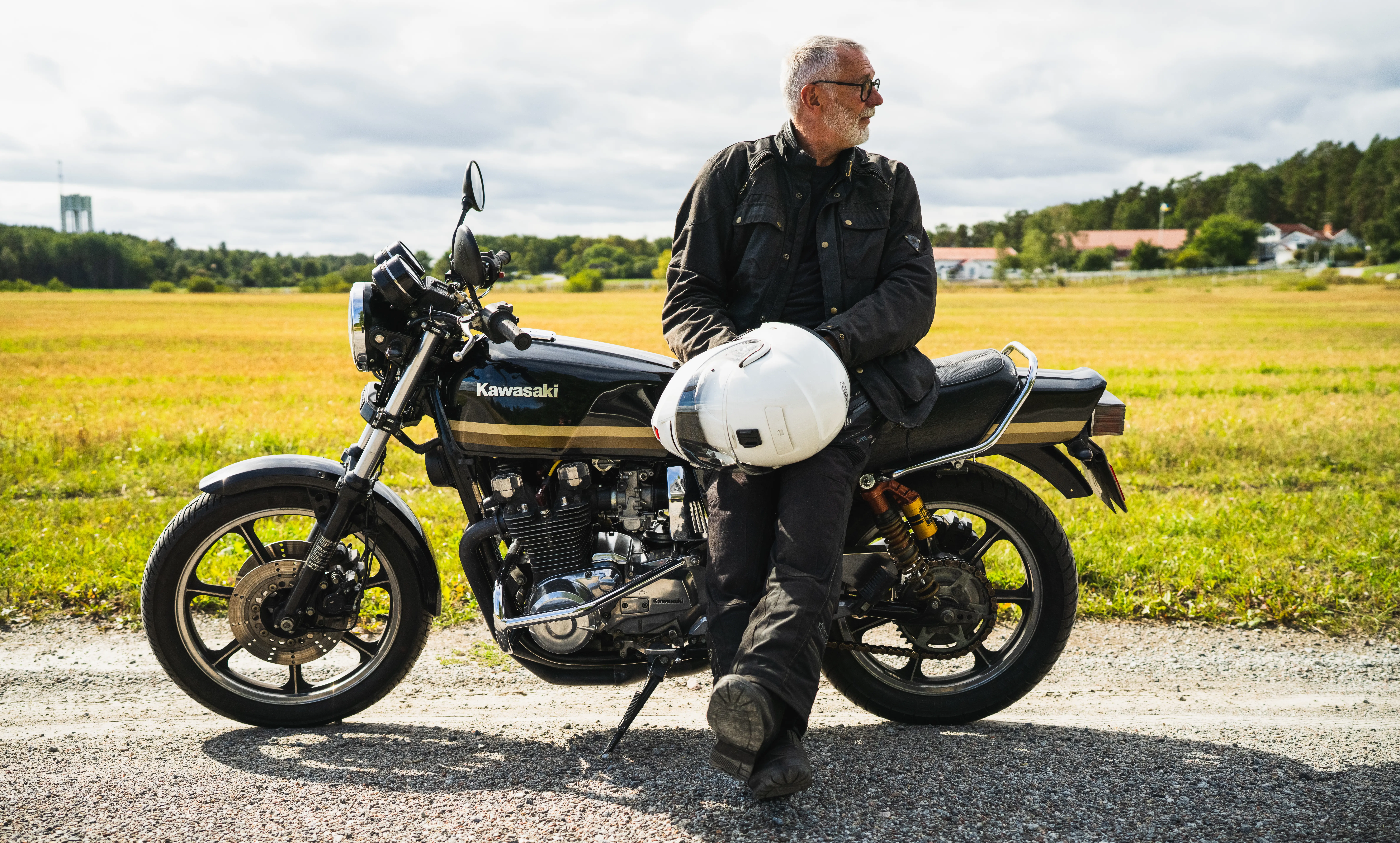 Äldre man lutar sig mot sin motorcykel på en landsväg
