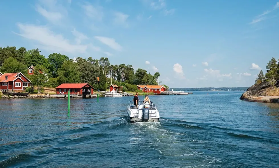 Båt som är ute på sjön med gröna sjömärken till höger i vattnet. 