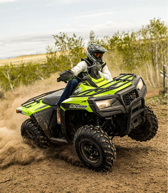 Person kör grön ATV från Arctic Cat i terräng med dammoln bakom.