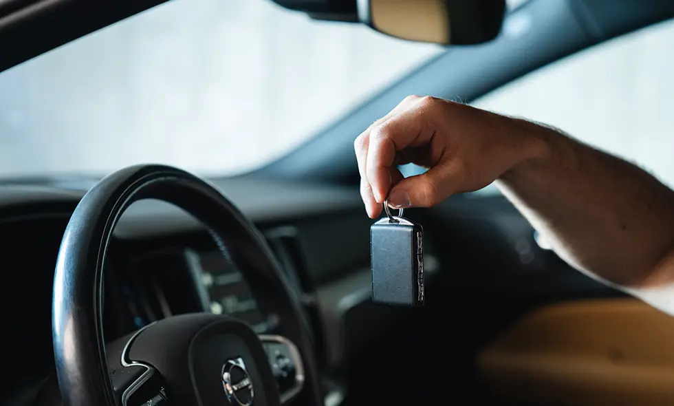 En person håller upp en svart bilnyckel inuti en bil, med ratten och interiördetaljer i bakgrunden.