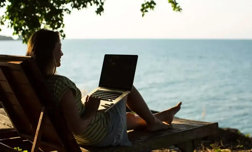 en kvinna jobbar med sin dator på en strand