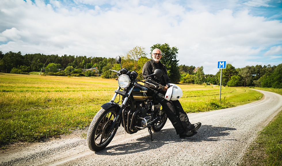 Äldre man lutar sig mot sin motorcykel på en landsväg