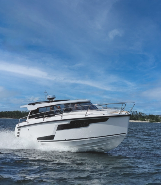 Motorbåt av märket Aquador färdas snabbt över vattnet nära en kustlinje med träd i bakgrunden.