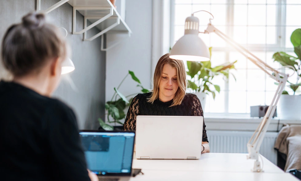 Två kvinnor framför en dator i en ljus arbetsmiljö, den ena med fokus på skärmen 