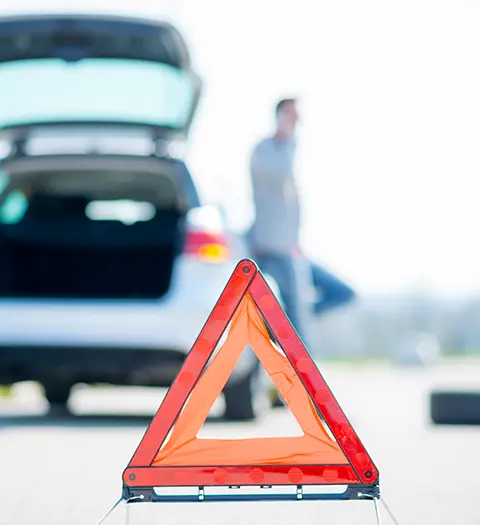 Varningstriangel framför öppen bil med person i bakgrunden.