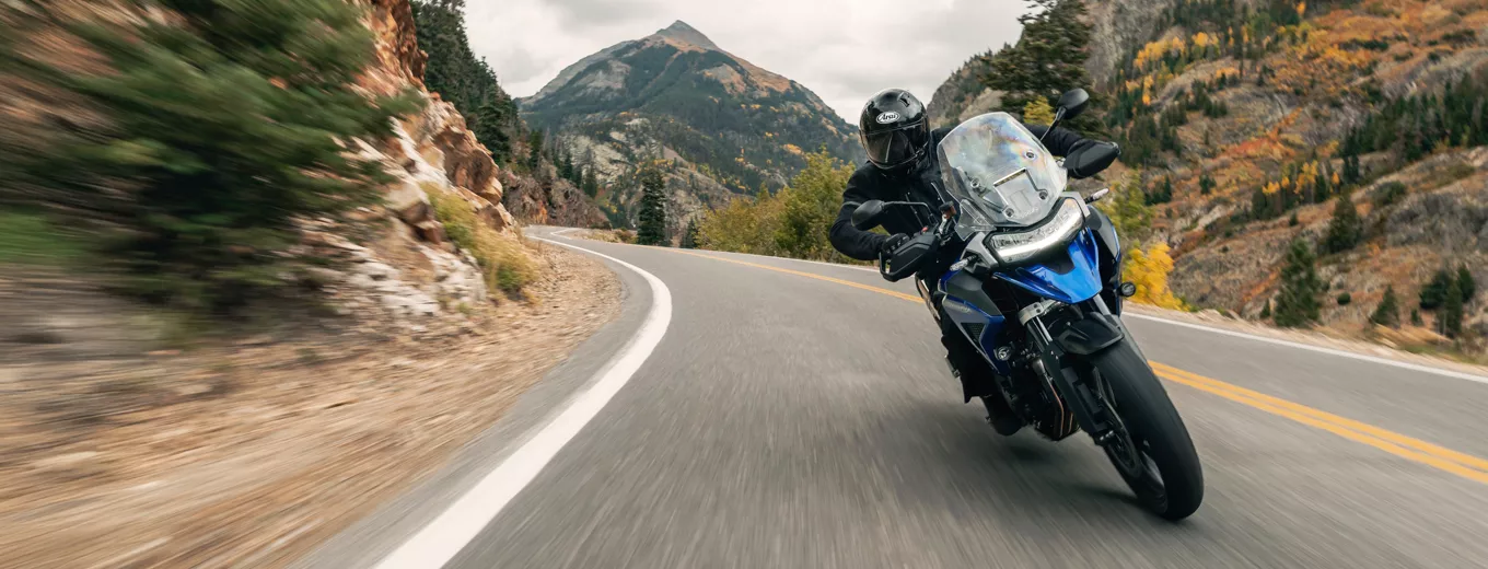 Motorcyklist kör på landsväg med berg och naturlandskap i bakgrunden.