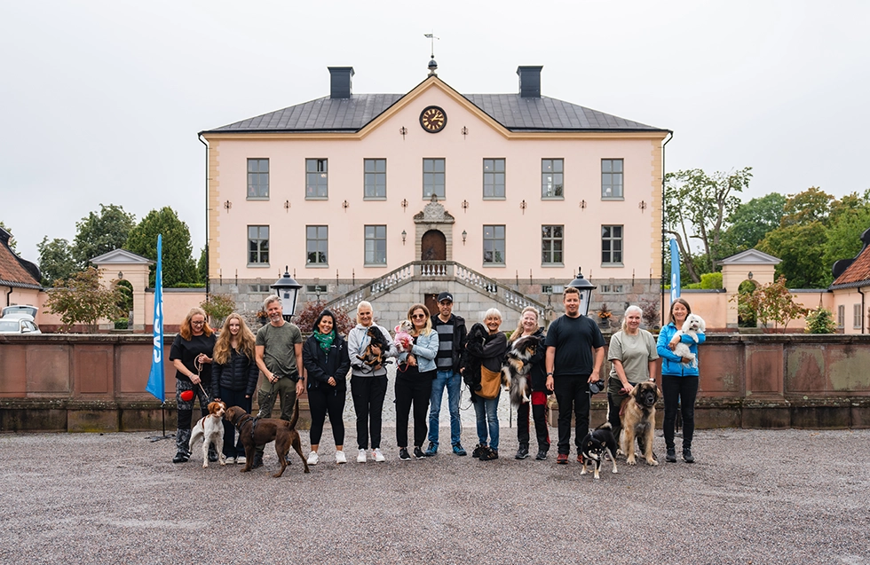 En gruppbild med flera människor tillsammans med deras hundar framför ett slott.)