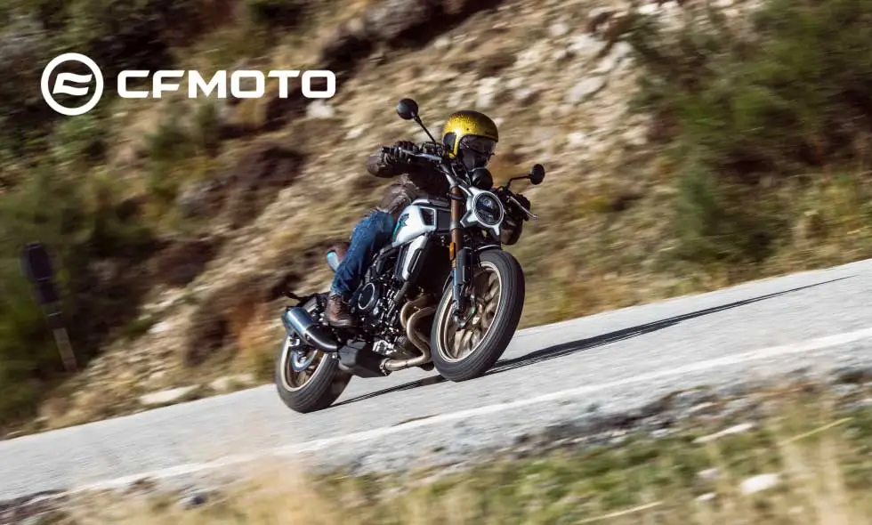 En motorcyklist i gult kör på en svart CFMoto motorcykel längs en bergig väg, med ett dramatiskt landskap i bakgrunden
