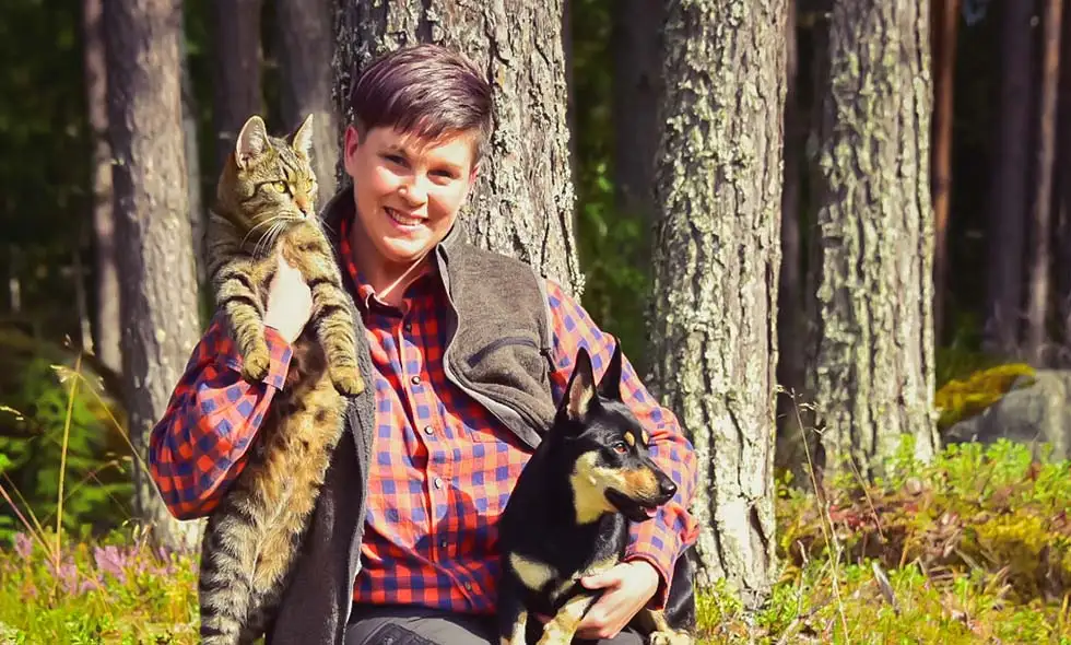 Kvinna i skogen håller en katt och en svart hund