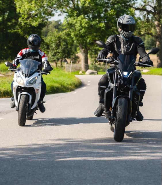 Två motorcyklister åker på en landsväg genom en lantlig miljö, den ena på en vit och svart sportmotorcykel och den andra på en svart cruiser