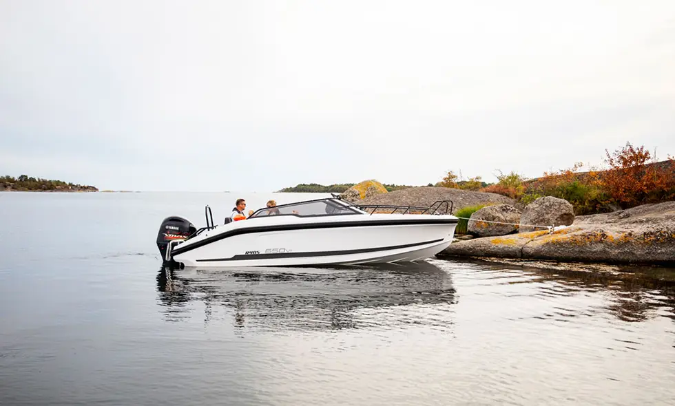 Motorbåt med två personer vid klippig kust i lugnt vatten.