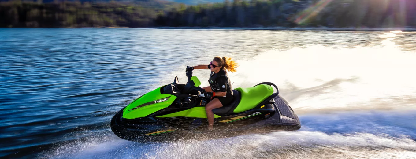 Kvinna kör en grön vattenskoter av märket Kawasaki snabbt på en sjö med skog i bakgrunden.