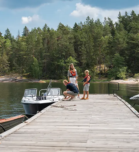 Familj står på brygga med båt bredvid en fin sommardag