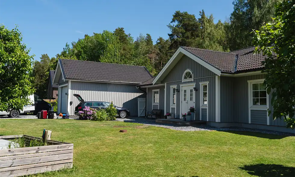 Grått trähus med vita detaljer och matchande garage under blå himmel. En bil med öppen lucka står parkerad på uppfarten.