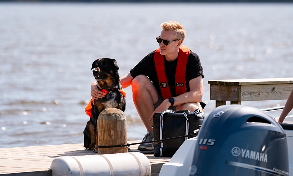 Människa på brygga med sin hund, båda i flytväst. 