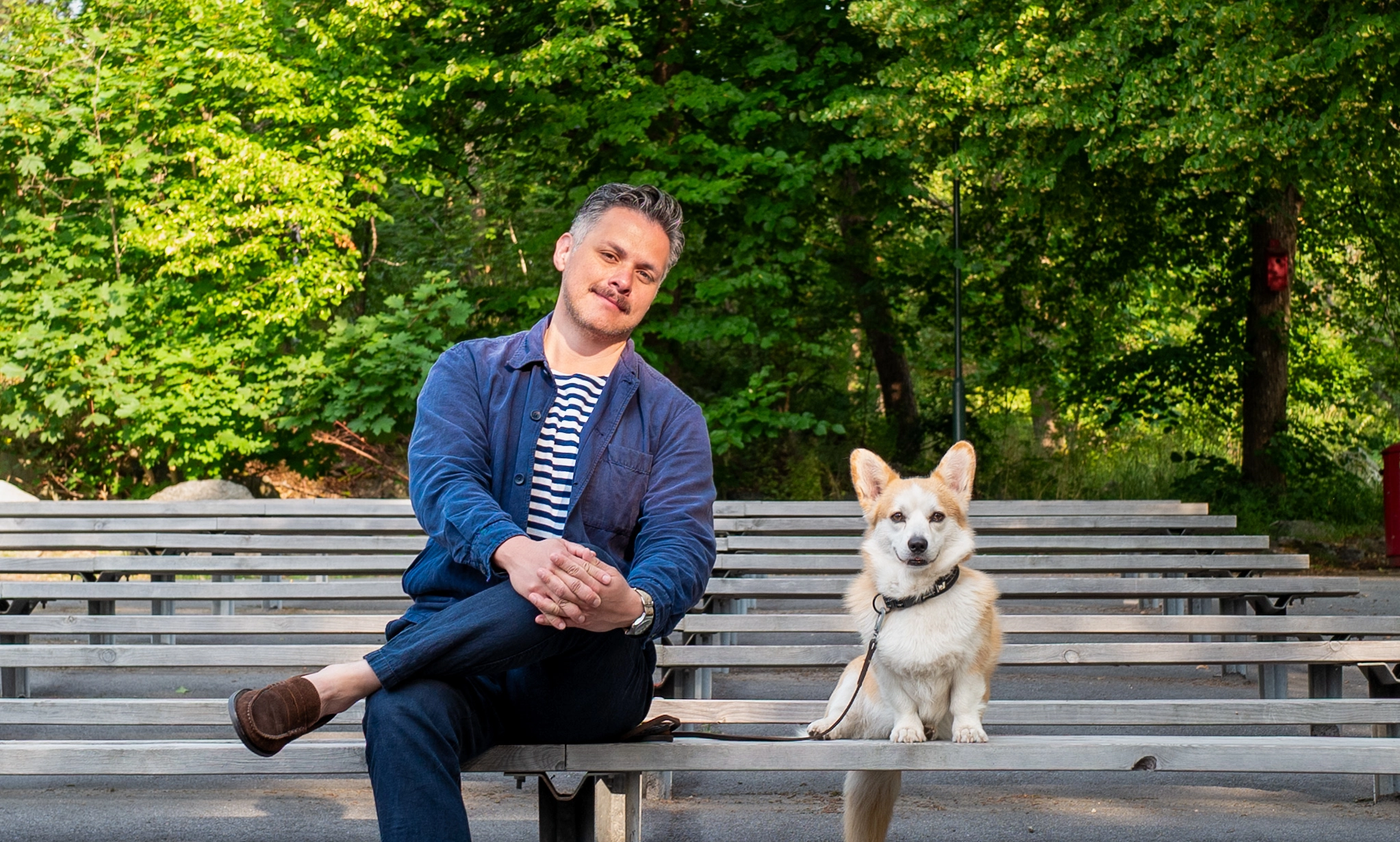 Hundägare sitter på en bänk utomhus tillsammans med sin Corgi-hund