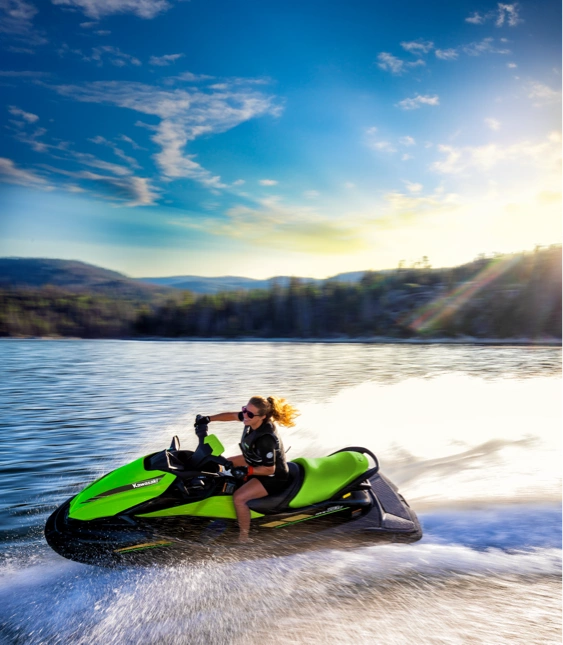 Kvinna kör en grön vattenskoter av märket Kawasaki snabbt på en sjö med skog i bakgrunden.