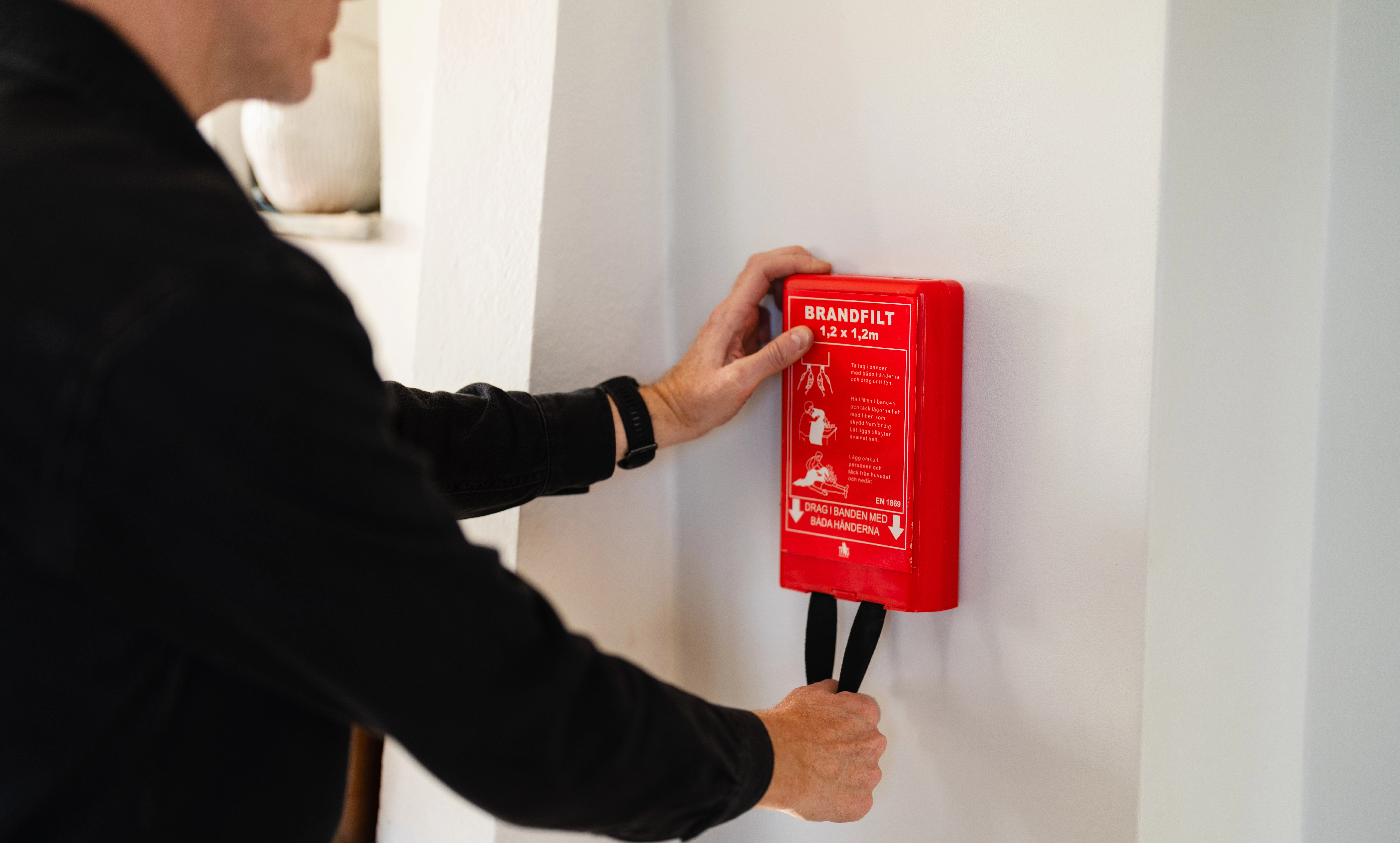 Person som håller i en brandfilt som sitter på väggen )