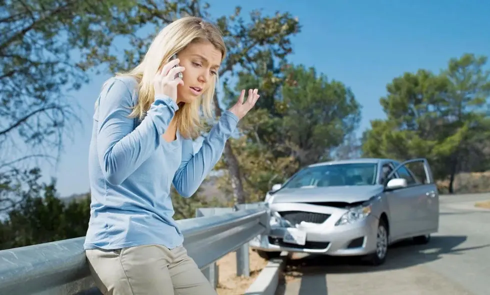 En kvinna pratar i telefon bredvid en krockad bil