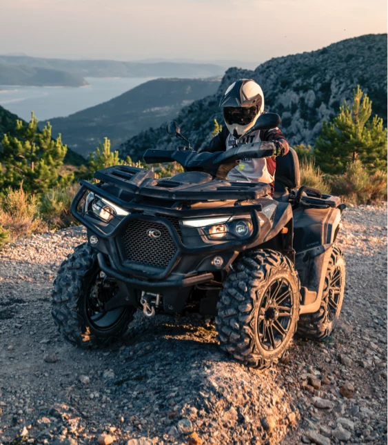 Person på svart ATV från Kymco stannar på grusväg i bergslandskap.