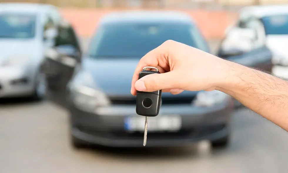 Hand håller upp bilnyckel framför parkerade bilar i dagsljus