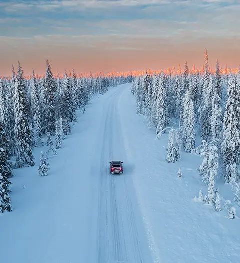 Bil kör på snötäckt väg omgiven av frostiga träd.