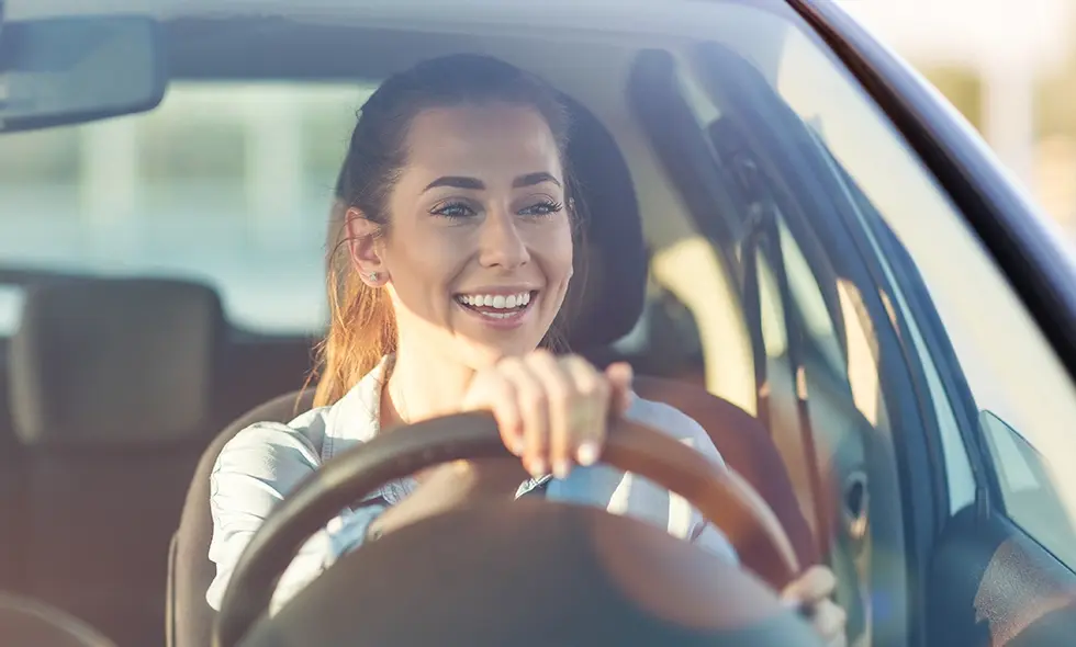 En glad kvinna som kör en bil och ler medan hon håller i ratten