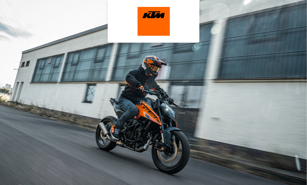 En person kör en orange och svart KTM-motorcykel i hög fart genom industriområde.