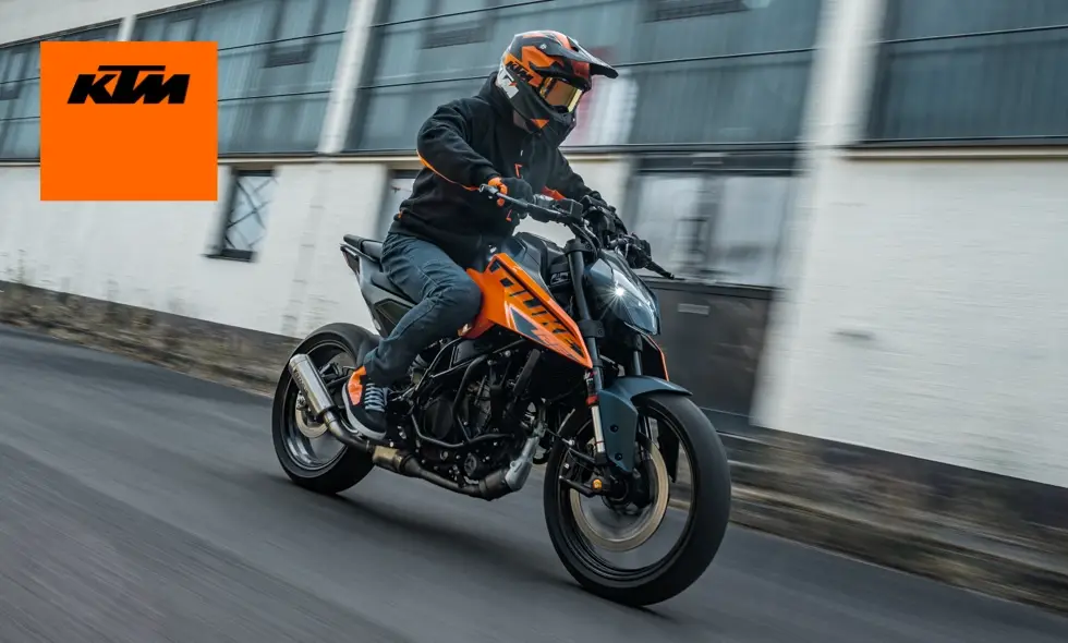 En motorcyklist kör en orange och svart KTM motorcykel i hög fart på en stadsgata, med suddig bakgrund som ger en känsla av rörelse