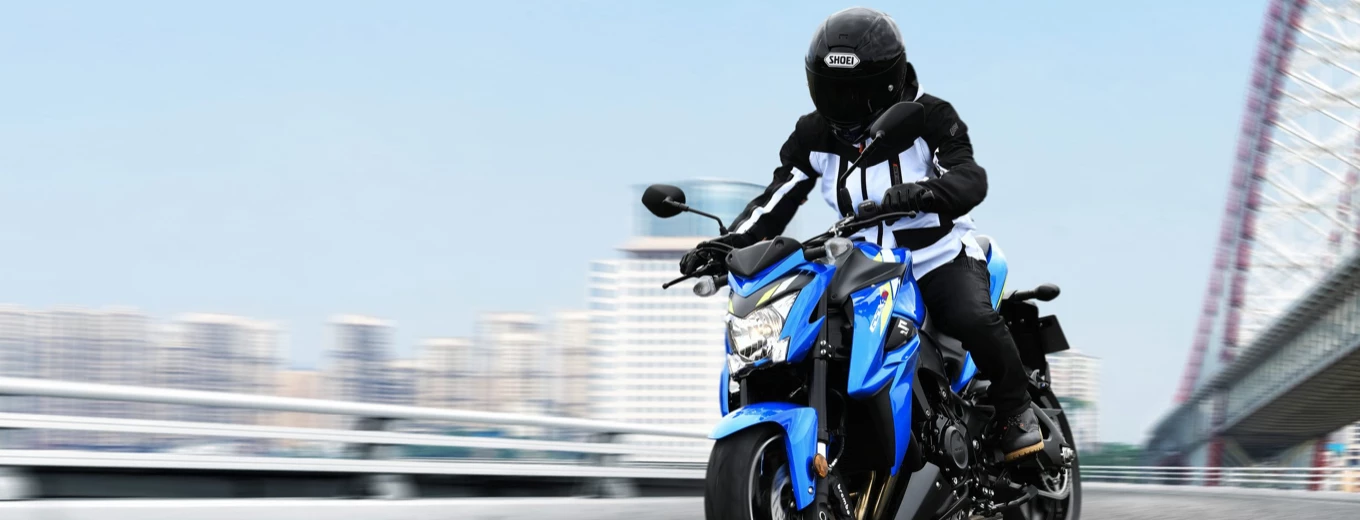 En motorcyklist i full skyddsutrustning styr en blå och vit sportmotorcykel på en bro