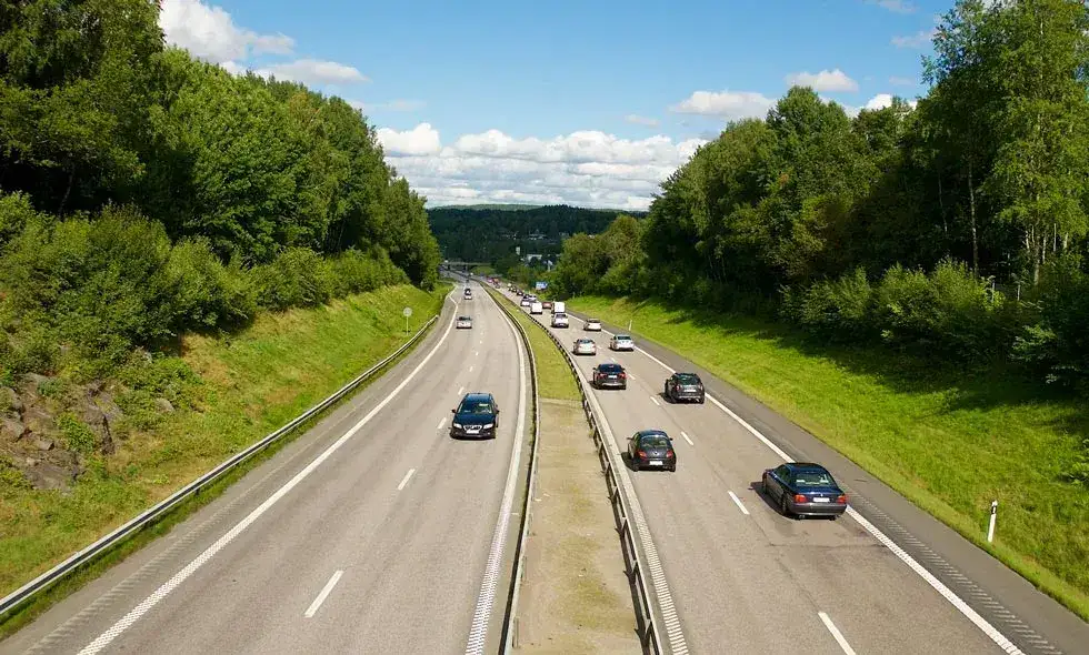 Bilar kör på en motorväg omgiven av gröna träd under en klar himmel