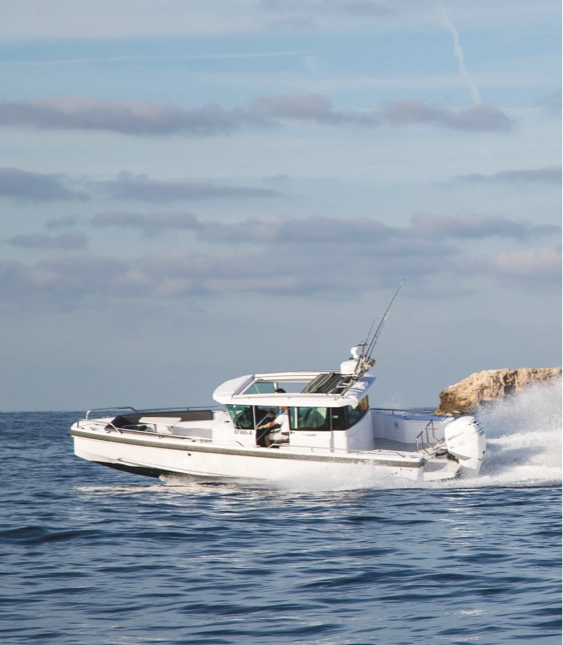 Motorbåt av märket Axopar med fiskespön på taket kör snabbt nära en klippa på öppet vatten.